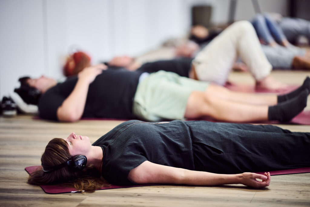 Mehrere Personen liegen entspannt in Rückenlage auf dem Boden während einer Entspannungs- oder Yoga-Phase